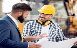 Two engineers with blueprint plan at construction site.