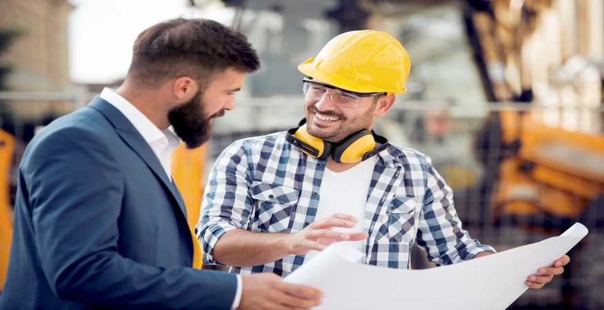 Two engineers with blueprint plan at construction site.